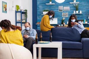 Group of multi ethnic antisocial friends keeping social distancing browsing on smartphones in apartment living room during global pandemic with coronavirus. photo