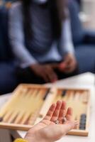 Cheerful happy woman using dice playing backgammon with multiethnic friends wearing face mask as prevention for covid 19 spread, during global pandemic sitting on couch drinking beer and eating popcorn. photo