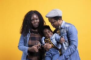 African american positive couple posing with their young child in studio, smiling people hugging together. Happy affectionate mom and dad showing gratitude and respect on camera. photo