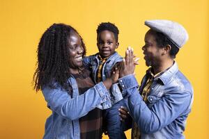 Happy black family sharing a high five together in the studio, feeling cheerful and showing affection to each other. African american couple with a small toddler posing with gratitude. photo