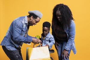 Curious little boy searching shopping bags for toys in the studio, looking for fun activities while his parents and playing with him. Happy african american family of three posing on camera. photo