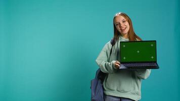 Smiling woman presenting laptop with green screen display, isolated over blue studio background. Cheerful person creating promotion with chroma key notebook device, camera B photo