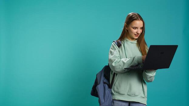 Joyful woman adding payment method on website using laptop, enjoying sales period, studio background. Girl doing purchases on internet, typing credit card information on notebook, camera B photo