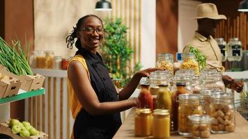 African american vendor arranging bulk products at local store, promoting zero waste concept for sustainable lifestyle. Merchant smiling and preparing to welcome clients at bio shop. Camera 1. photo