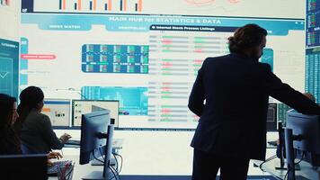 General director CEO sharing insight about a new development strategy with his employees, showing important data reports to analyze organizational activity status in a control room. Camera B. photo