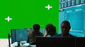 Diverse group of business specialists solve their daily tasks in control room with big greenscreen, analyzing big data numbers to ensure organizational progress. Startup management team. Camera A. photo