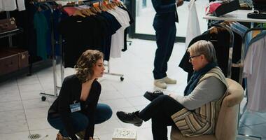 Elderly woman searching for a comfortable pair of shoes at mall, asking retail assistant about available sizes. Store employee recommending various footwear models for senior client. Camera B. photo