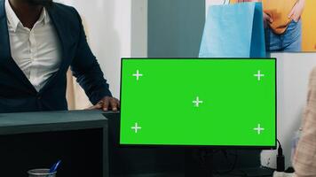 African american worker uses computer with greenscreen display on at checkout counter, putting clothes in a bag for customer. Employee looks at pc showing copyspace mockup screen. Camera A. photo