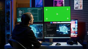 Hacker using green screen monitor and artificial intelligence to write spyware software gathering data from users. Scammer in apartment using AI and mockup PC display to do fraud using AI, camera A photo