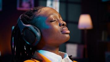 Carefree student finishes creating a presentation and relaxes with music on audio headset, resting after long researching session. African american girl chilling with ambience tunes. Camera B. photo