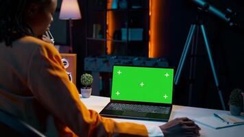 Young woman using laptop with isolated greenscreen display at her home office, resolving homework tasks for university courses. Student looking at blank copyspace chromakey on pc. Camera B. photo