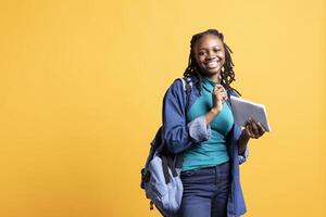 Portrait of cheerful young girl smiling, reading and writing for school exam on notepad, studio background. Joyous student holding exercise notebook with research done for university courses photo