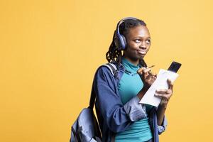 BIPOC student thinking how to solve homework exercises while listening music, isolated over studio background. Girl studying for exam, contemplating and enjoying songs on headphones photo