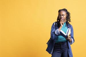 African american woman with book in hands deep in thoughts, isolated over yellow studio background. Bookworm holding novel, thinking about themes and characters after reading photo