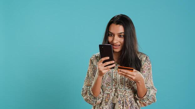 Woman adding payment method on phone website, delighted to take advantage of promotions, studio background. Person thrilled to do internet shopping, typing credit card data on smartphone, camera A photo