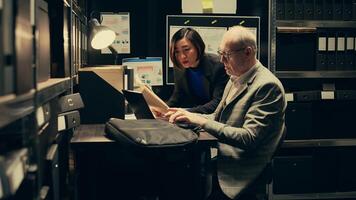 Team members cross reference data to track down potential suspect, using archived records and forensic evidence reports. Officers uncover crucial information to help solve legal case. Camera B. photo