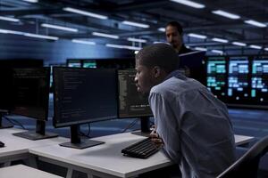IT engineer in server room facility confused by errors on screen while shielding data from potential threats. Perplexed man puzzled by bugs while safeguarding data center hardware against malware photo