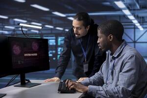 Team of developers in server hub trying to protect hardware from hacker stealing information. Coworkers in data center workplace trying to fix security breach alert caused by virus photo