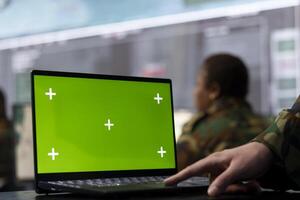 Trooper utilizing chroma key mockup screen on a laptop in military headquarters, providing real time data to ensure national safety. High ranking serviceman uses pc with copy space display. photo