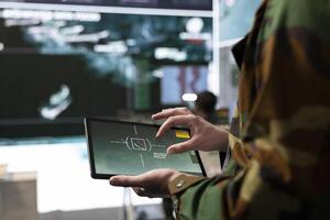 Military IT engineer collecting intelligence from world map projection, tablet connected to radar CCTV system to support soldiers in the field. Dispatch federal defense agency control room. Close up. photo