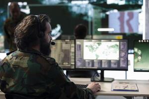 Military staff monitoring real time battlefield operation from CCTV radar system in command center, collecting information for an infantry unit support. Satellite high tech specialist in power base. photo