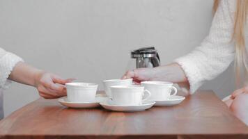Hand reaching for a coffee cup on a wooden table with a coffee pot in the background. video