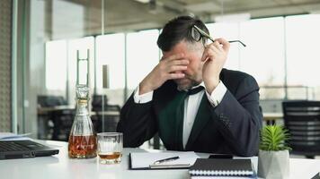 Depressed drunk senior businessman sitting at computer with alcohol. Old tired employee overwhelmed with tasks in office video