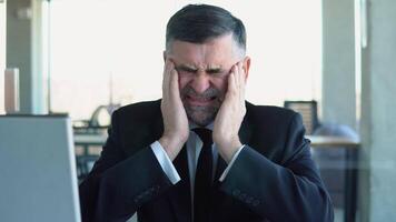 Old tired employee overwhelmed with tasks in office. Depressed senior businessman sitting at computer video