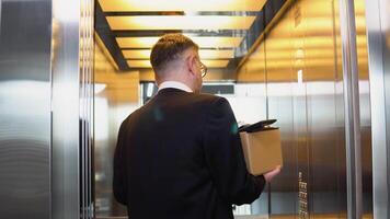 Sad dismissed senior worker with carton dismissal box getting into the elevator. Old man is retiring. Retirement concept. Dismissal from work, s3niorlife video