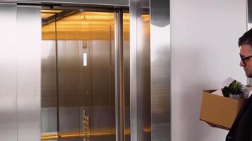 Sad dismissed senior worker with carton dismissal box getting into the elevator. Old man is retiring. Retirement concept. Dismissal from work video