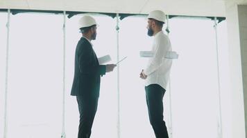 indiano e árabe arquitetos construtores encontro às construção local. dois multiétnico engenheiros discutindo em plano. dois construção trabalhadores trabalhando juntos enquanto visitando uma Novo construção video