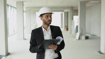 Indian asian builder engineer worker in helmet walking at construction site of skyscraper video