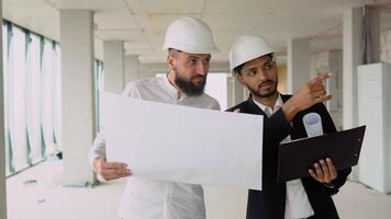 Indian architect and arabian supervisor meeting at construction site. Multiethnic engineers discussing on plan. Two construction workers working together while visiting a new building video