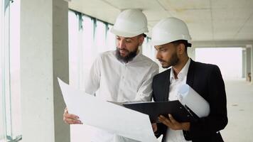 Indian architect and arabian supervisor meeting at construction site. Multiethnic engineers discussing on plan. Two construction workers working together while visiting a new building video