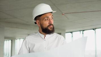 Serious attractive arabian industrial engineer in hard hat with project drawings at construction of a skyscraper. Professional and industry, builder architect job, worker checking work at plant indoor video