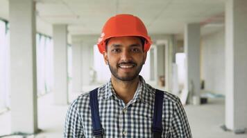 Portrait of Indian worker builder in uniform wearing a safety helmet looking at the camera, standing on construction site video