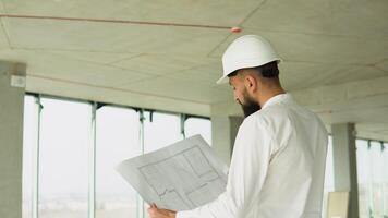 sério atraente turco industrial engenheiro dentro Difícil chapéu com projeto desenhos às construção do uma arranha-céu. profissional e indústria, construtor arquiteto trabalho, trabalhador verificação trabalhos às plantar interior video