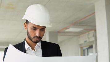 ásia engenheiro bonito homem ou arquiteto olhando construção plano com branco segurança capacete dentro construção local video