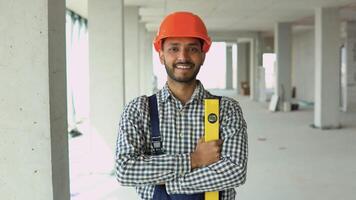 Portrait of Indian worker builder in uniform wearing a safety helmet with waterpas looking at the camera, standing on construction site of office center video