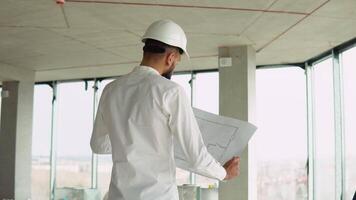 Serious attractive arabian industrial engineer in hard hat with project drawings at construction of a skyscraper. Professional and industry, builder architect job, worker checking work at plant indoor video