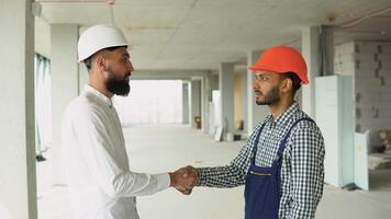 Indian worker and arabian architect in helmets handshake in a construction site. Two engineer shaking hands with deals and congratulations on success video