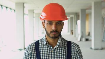 Portrait of Indian worker builder in uniform wearing a safety helmet looking at the camera, standing on construction site of office center video