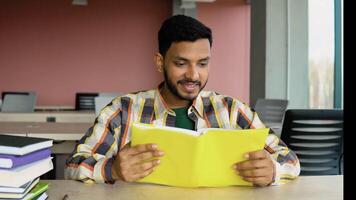 Indian student reads a book in library. Young asian student sitting at table doing assignments in college library video