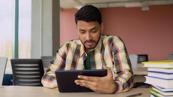 Indian smiling student using a tablet, study a simple Internet course, online learning in the application, write notes, prepare for the exam, watch educational . chat with the teacher video