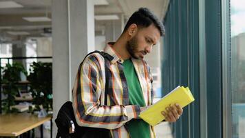 Portrait of Indian clever student with open book reading it in college library video