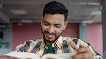 Indian student reads a book in library. Young asian student sitting at table doing assignments in college library video
