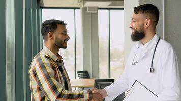 Indian patient and arabian doctor in white coat handshake in a medical clinic. Close up of medical multiethnic people handshake in a hospital video