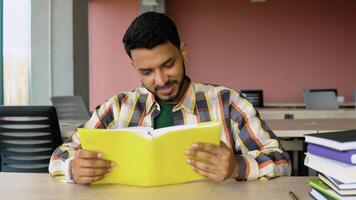 Indian student reads a book in library. Young asian student sitting at table doing assignments in college library video