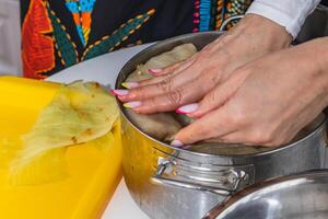 Women cook cabbage rolls while standing at the table and put them in a pot. photo