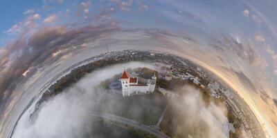 Aerial view from high altitude tiny planet in morning sky with clouds overlooking old town with castle in fog. Transformation of spherical 360 panorama in abstract aerial view. photo